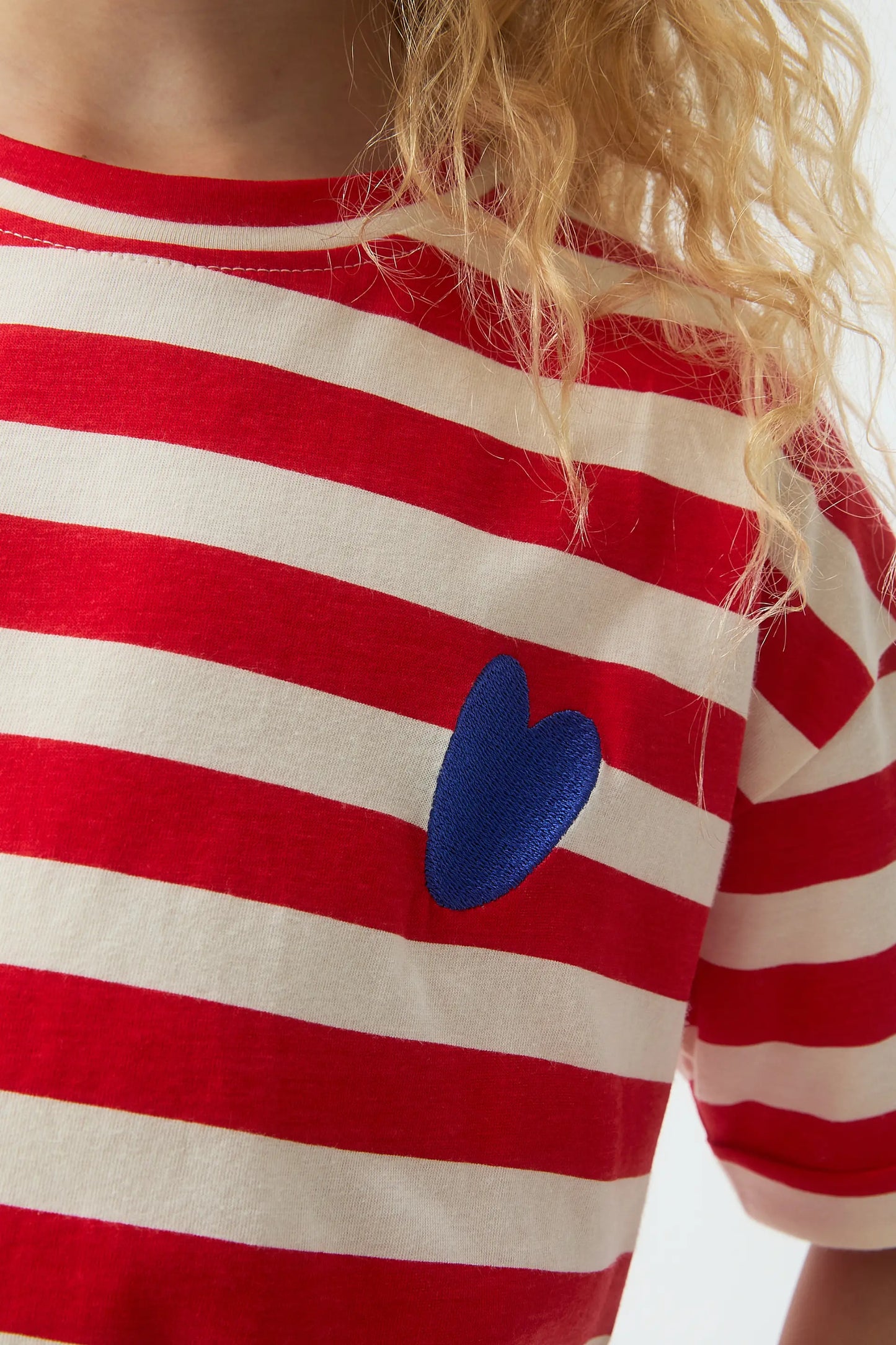 Maglietta da bambina con stampa a righe rosse e cuore ricamato.